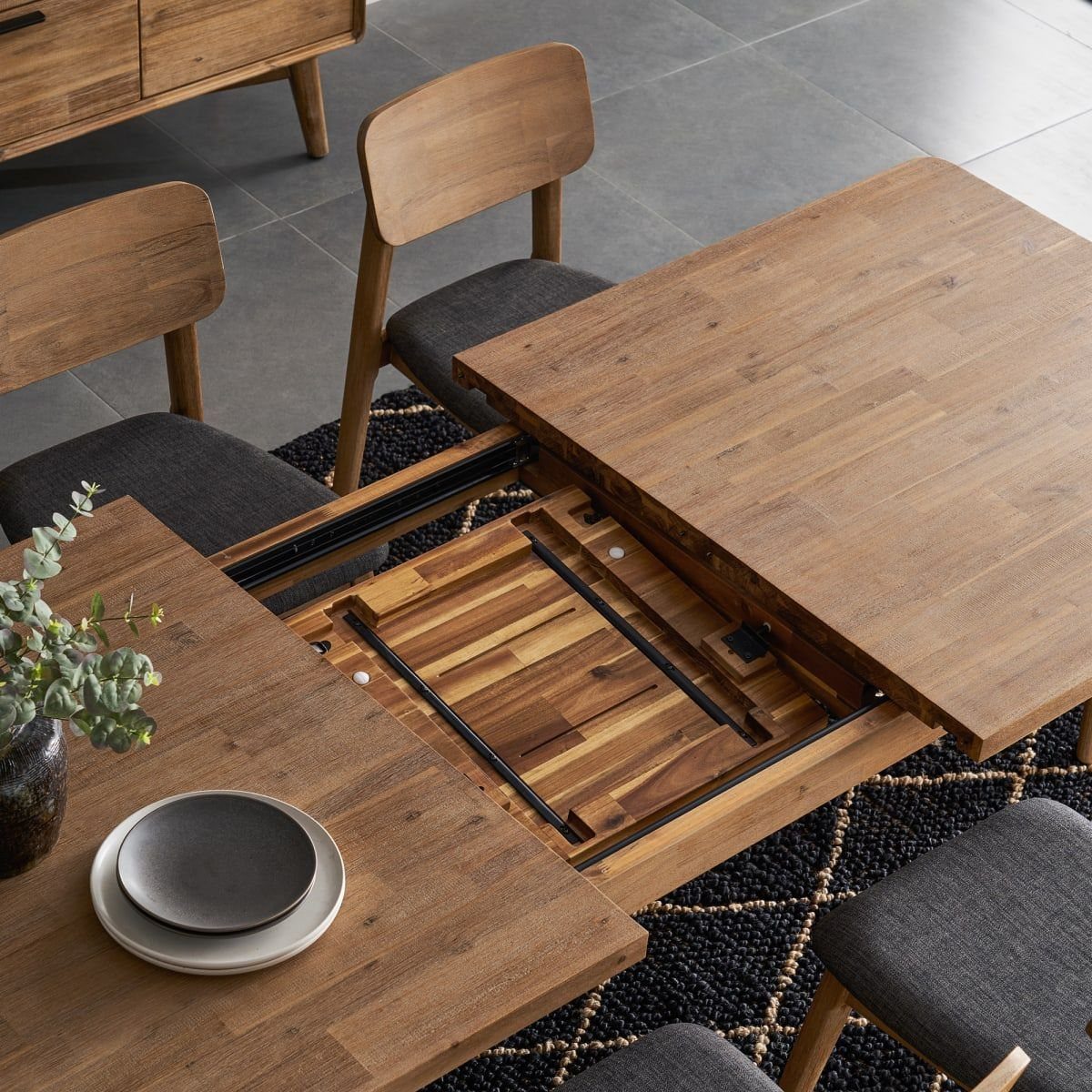 Wooden extendable dining table showing the internal leaf mechanism with grey upholstered chairs.