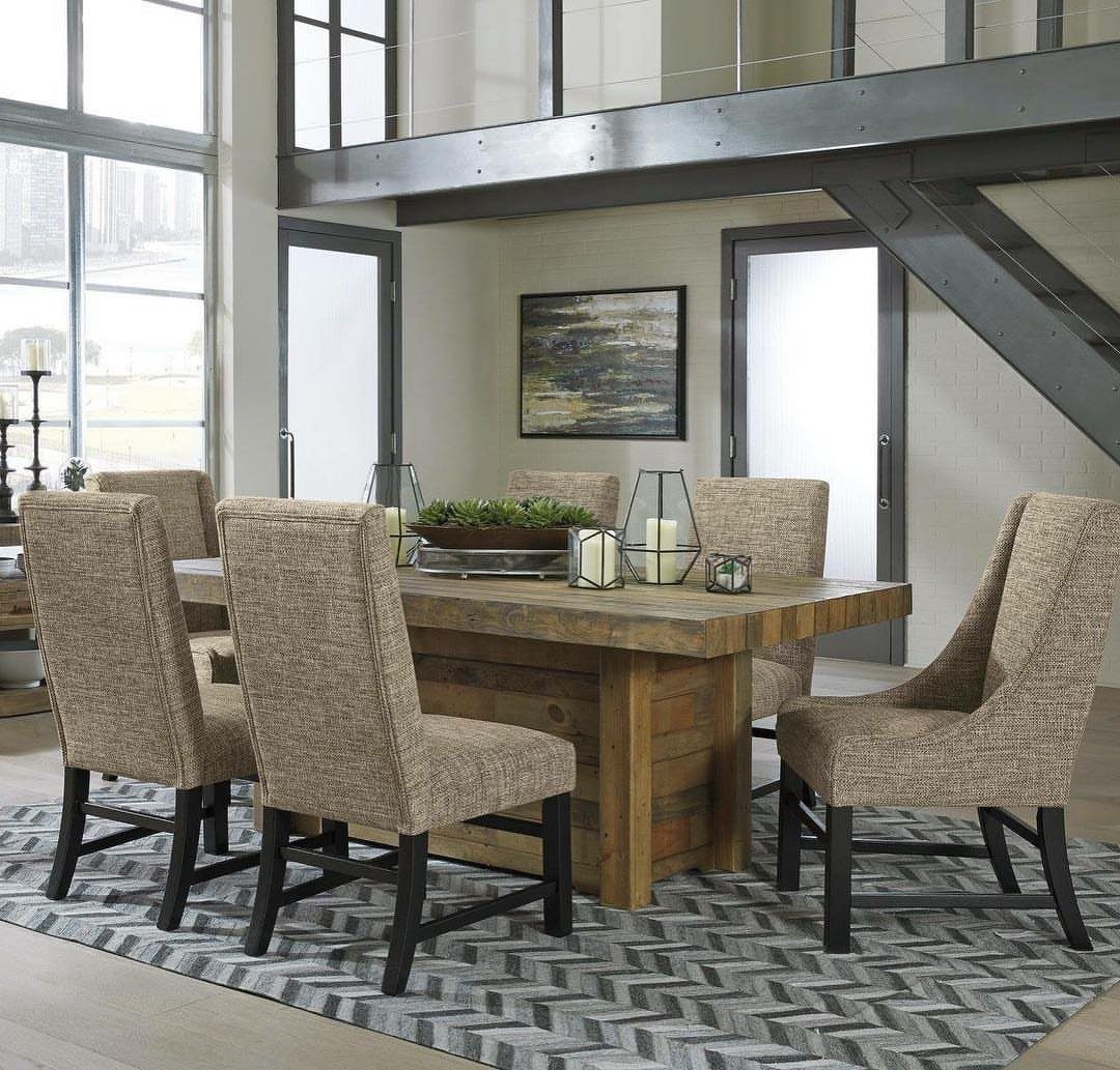 Beige upholstered dining chairs surrounding a rustic rectangular wooden table on a chevron rug.