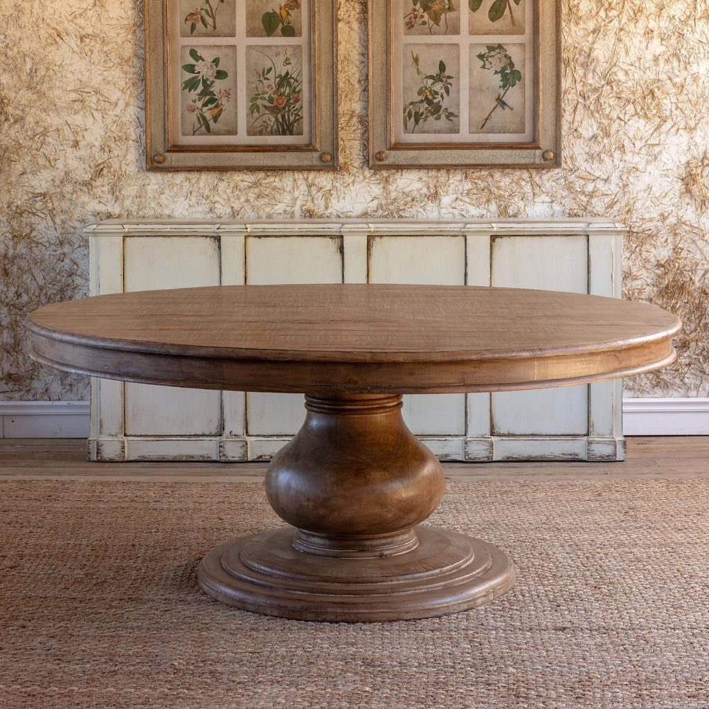 Round wooden dining table with pedestal base in a rustic interior setting
