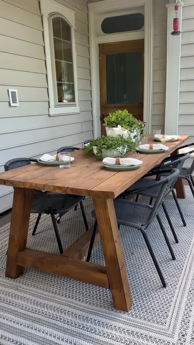 Wooden rectangular dining table with black chairs on a patterned outdoor porch rug