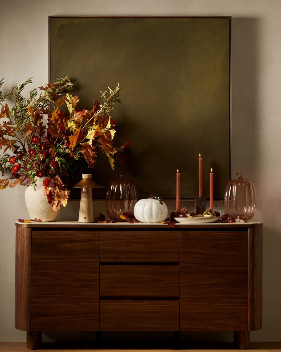 18 Autumn Dining Room Decor Ideas for a Warm and Inviting Space 18 Autumnal sideboard display with colorful leaves, pumpkins, and candles against a dark painting.