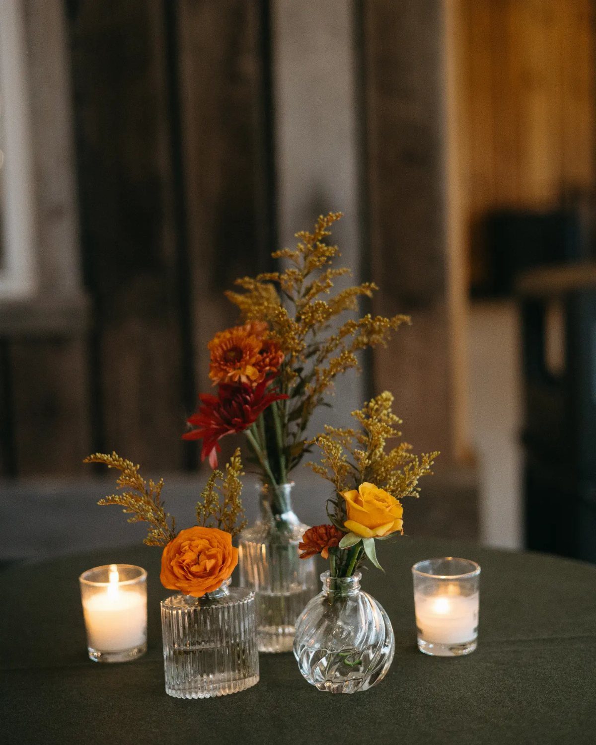 18 Autumn Dining Room Decor Ideas for a Warm and Inviting Space 14 Three glass bud vases with autumn flowers and tea light candles on dark tablecloth.