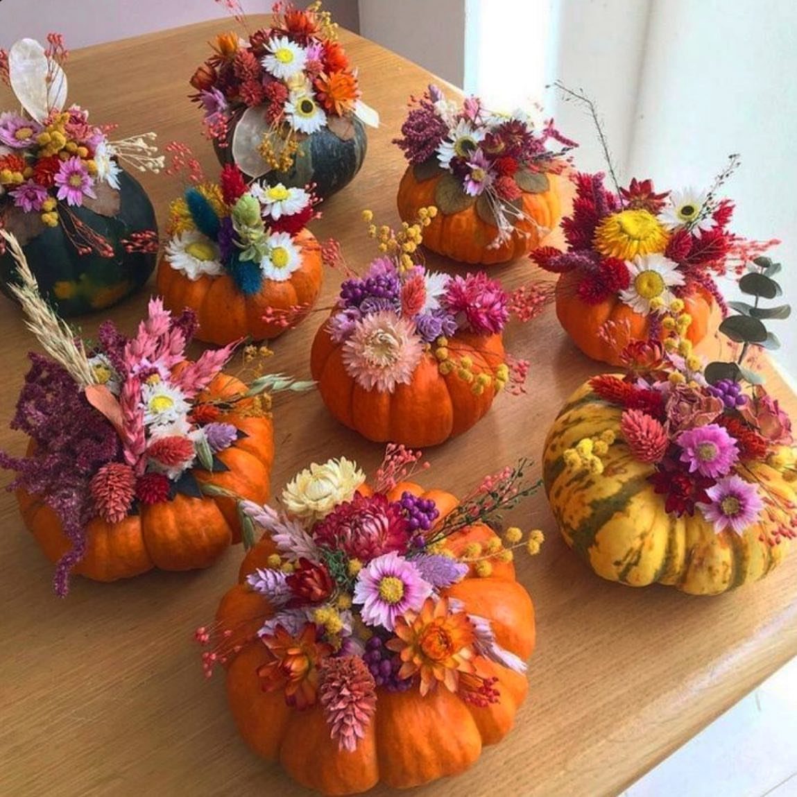 18 Autumn Dining Room Decor Ideas for a Warm and Inviting Space 2 Small pumpkins filled with colorful autumn flowers arranged on a light wooden table.
