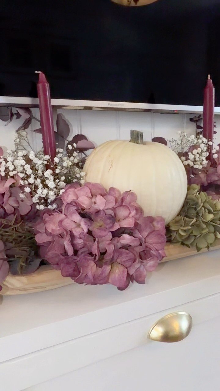 18 Autumn Dining Room Decor Ideas for a Warm and Inviting Space 6 Wooden dough bowl centerpiece with white pumpkin, purple flowers, and taper candles.