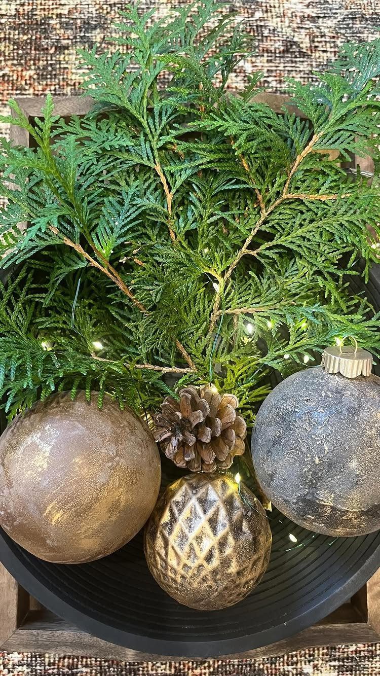 15 Christmas Coffee Table Decor Ideas for a Festive Home 1 Black bowl filled with gold and silver ornaments, cedar branches, and a pinecone.