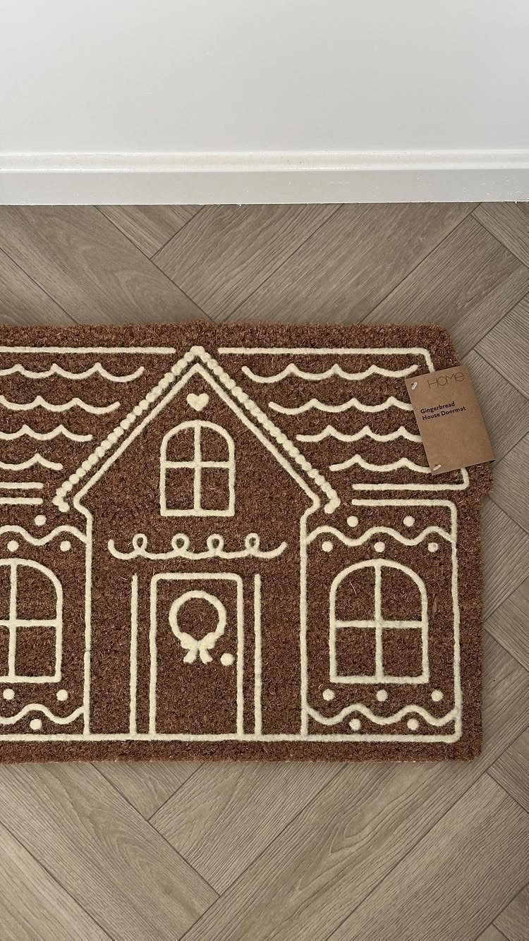 21 Christmas Decor Gift Ideas for the Holidays 12 Brown coir doormat with a white gingerbread house design on a wood floor.