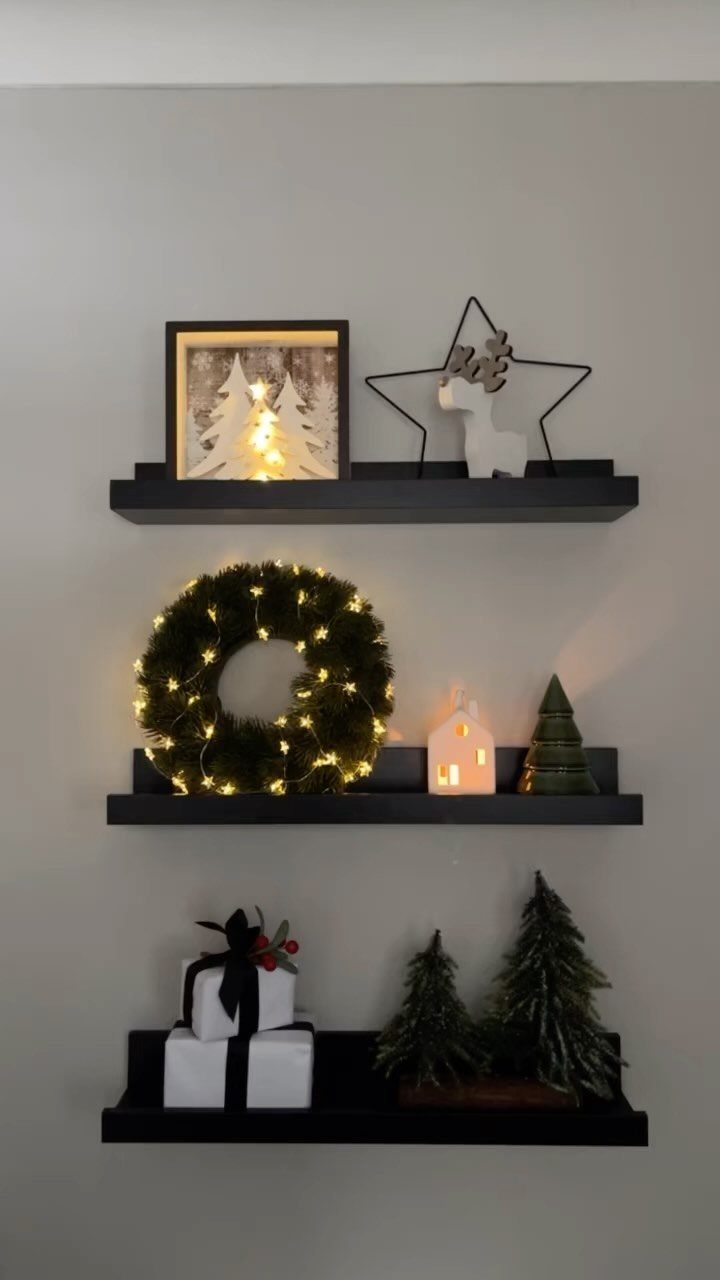 21 Christmas Decor Gift Ideas for the Holidays 8 Black picture ledges on a wall decorated with Christmas wreaths, trees, and gifts.