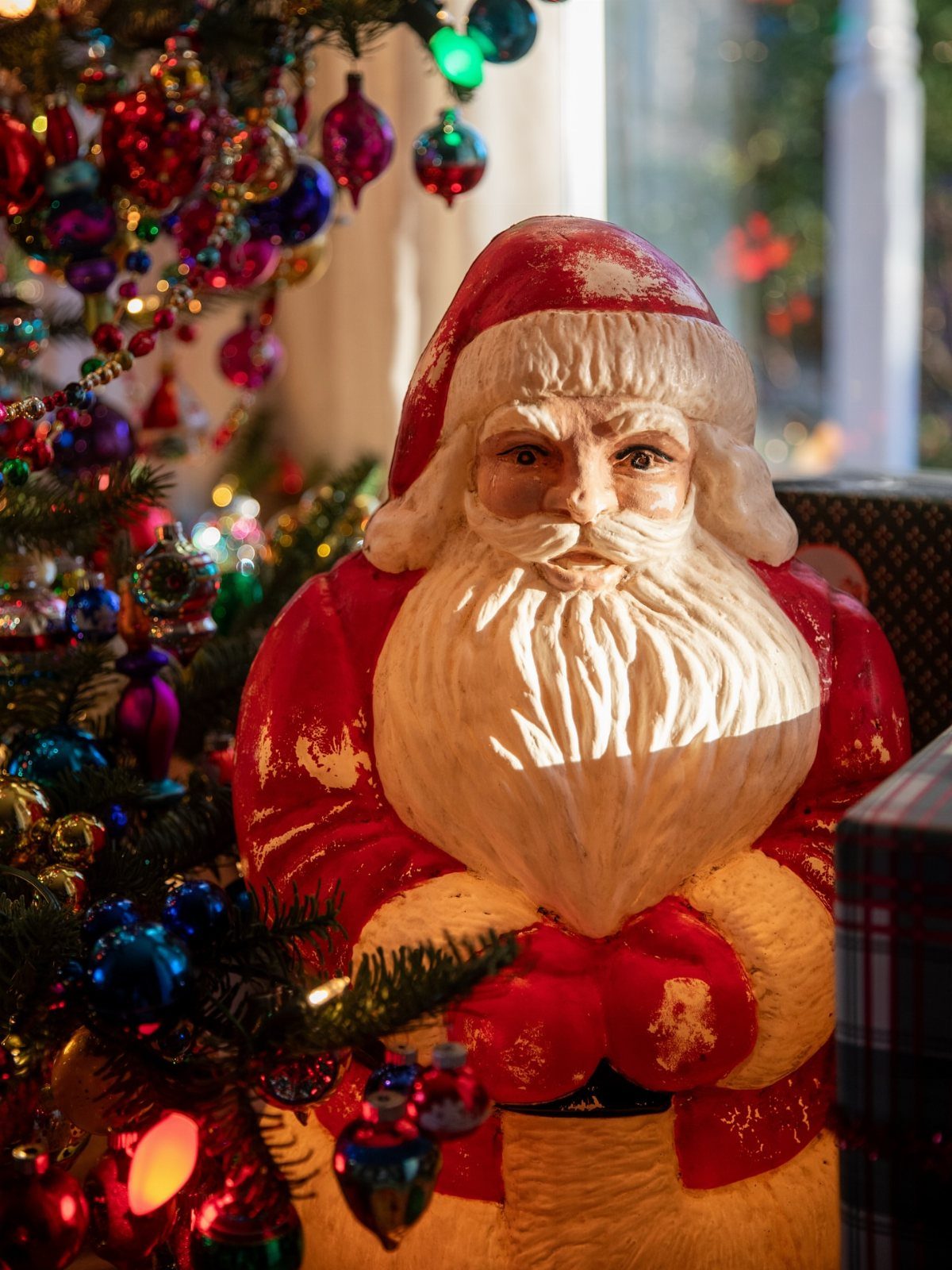 21 Christmas Decor Gift Ideas for the Holidays 21 Santa Claus figurine standing beside a Christmas tree decorated with colorful ornaments.