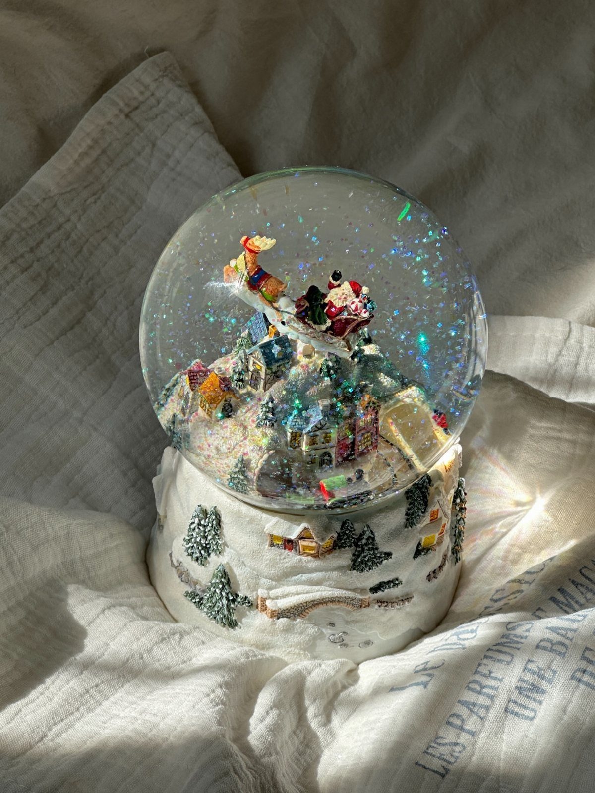 21 Christmas Decor Gift Ideas for the Holidays 14 Snow globe with Santa in a sleigh and a winter village on white fabric.