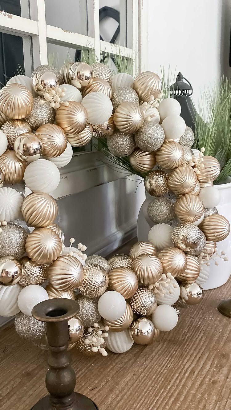 21 Christmas Decor Gift Ideas for the Holidays 1 Gold and white ornament wreath resting on a wooden table by a window.