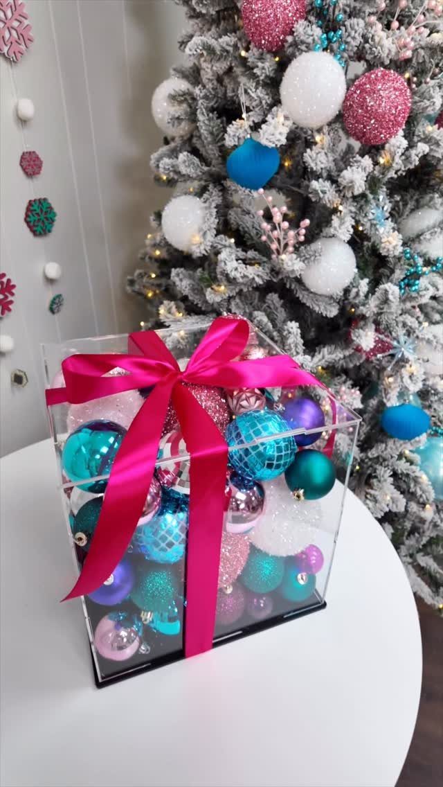 17 Christmas Decor Ideas with White for a Serene Home 9 Clear acrylic gift box filled with colorful ornaments and a pink ribbon bow.