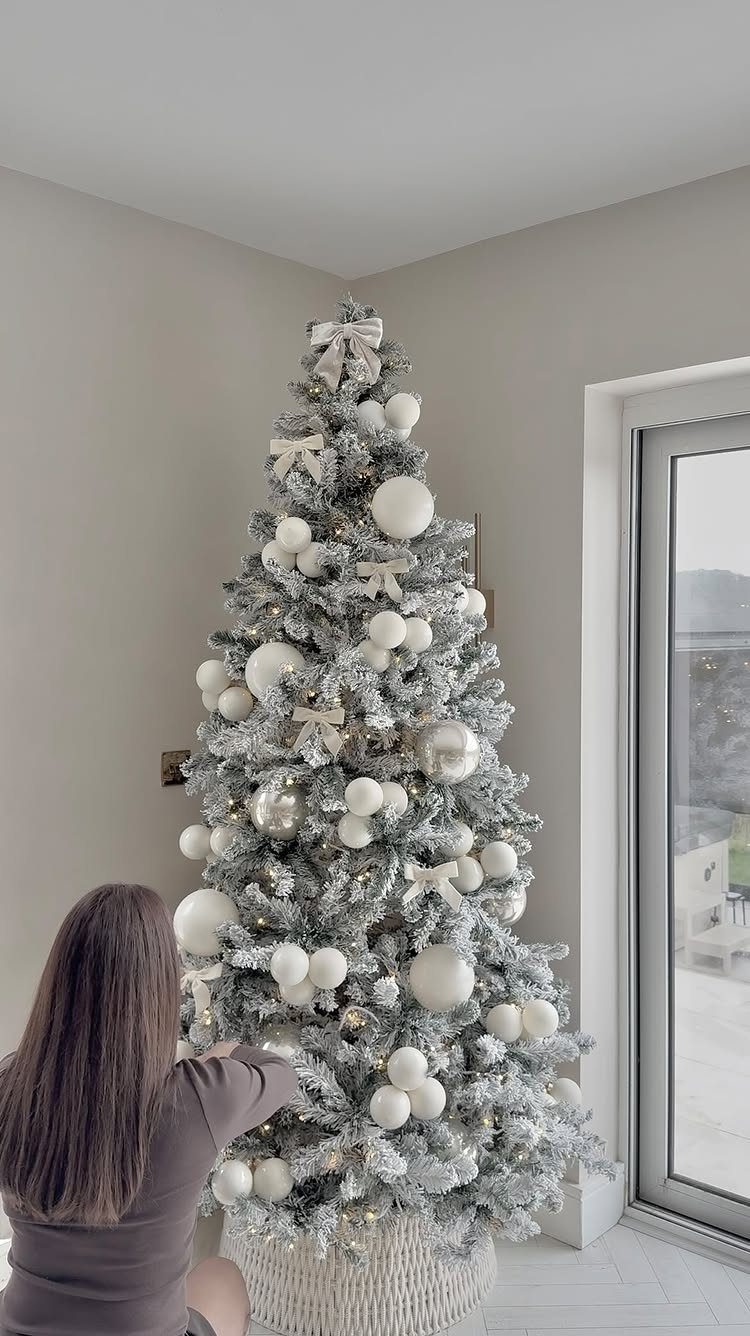 17 Christmas Decor Ideas with White for a Serene Home 1 Flocked Christmas tree decorated with white ornaments and bows in a bright room.