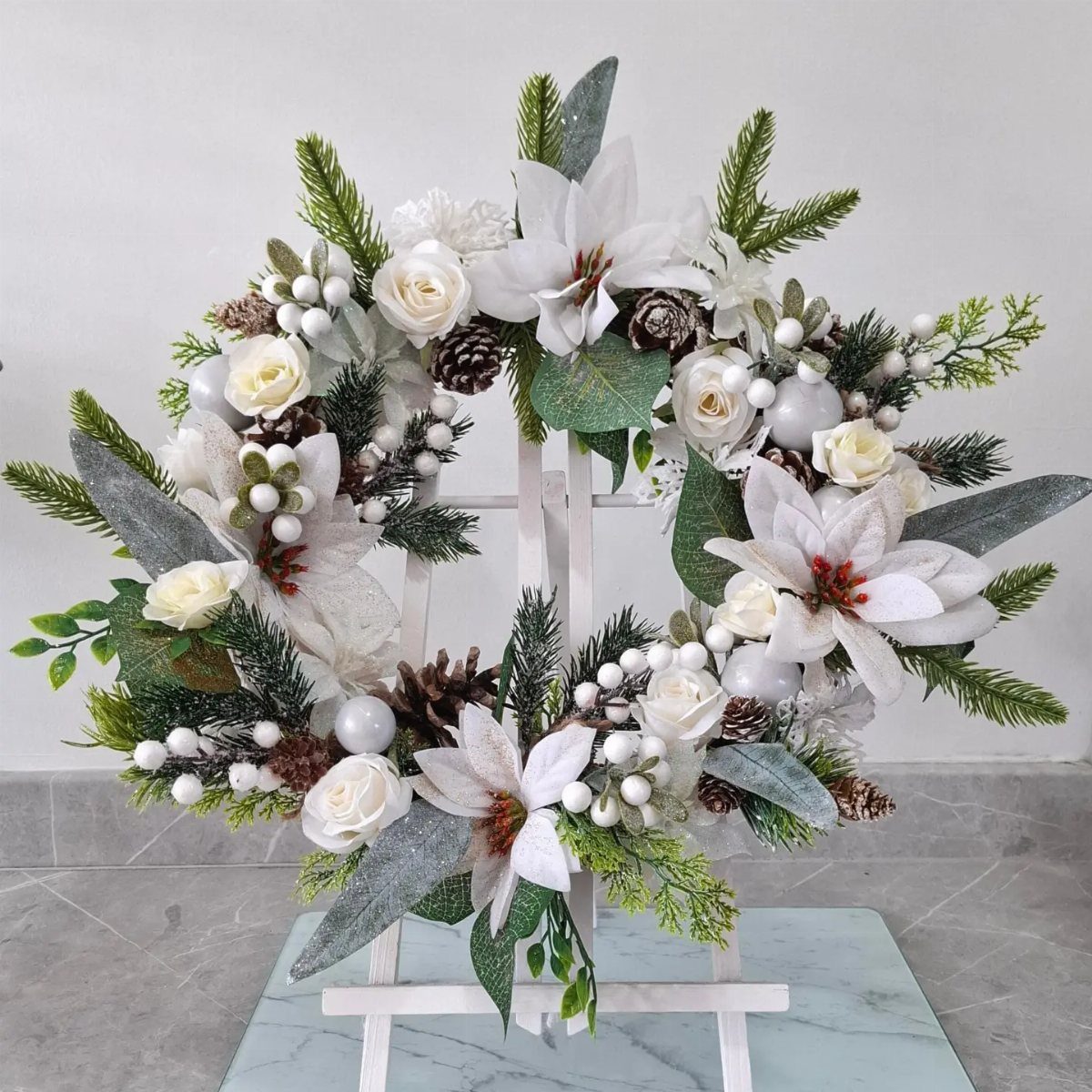17 Christmas Decor Ideas with White for a Serene Home 15 White Christmas wreath with roses, lilies, and frosted greenery on a white stand.