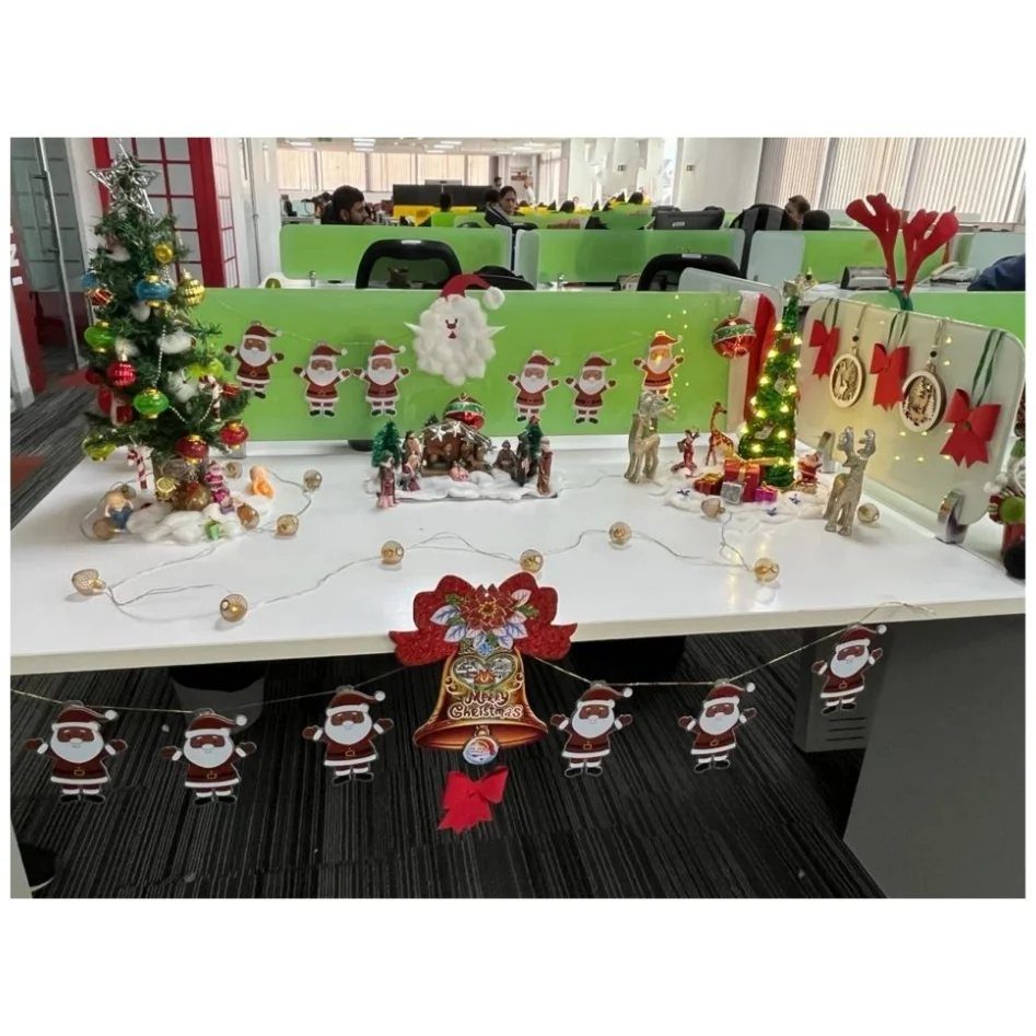 16 Christmas Decorations for Office Spaces That Shine 1 Christmas decorated office desk with mini tree, Santa cutouts, and festive string lights.