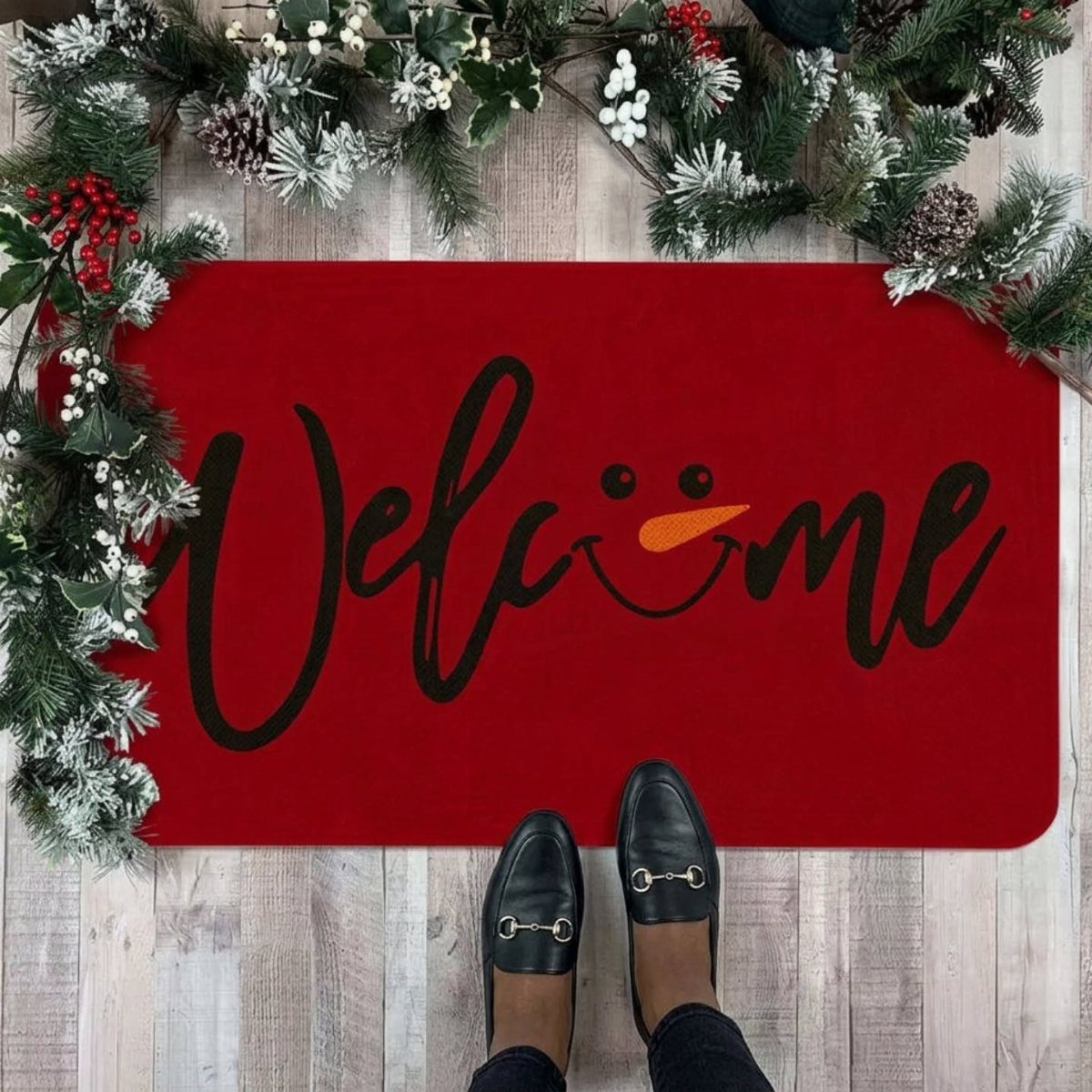 16 Christmas Decorations for Office Spaces That Shine 6 Red welcome mat with snowman face design surrounded by festive pine garlands on wood floor