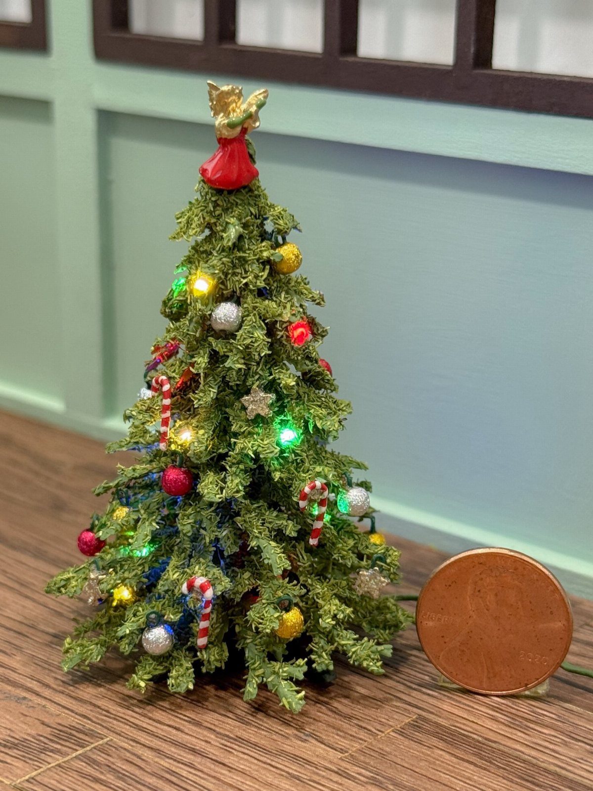 16 Christmas Decorations for Office Spaces That Shine 2 Small artificial Christmas tree with colorful ornaments and an angel topper on wooden surface.