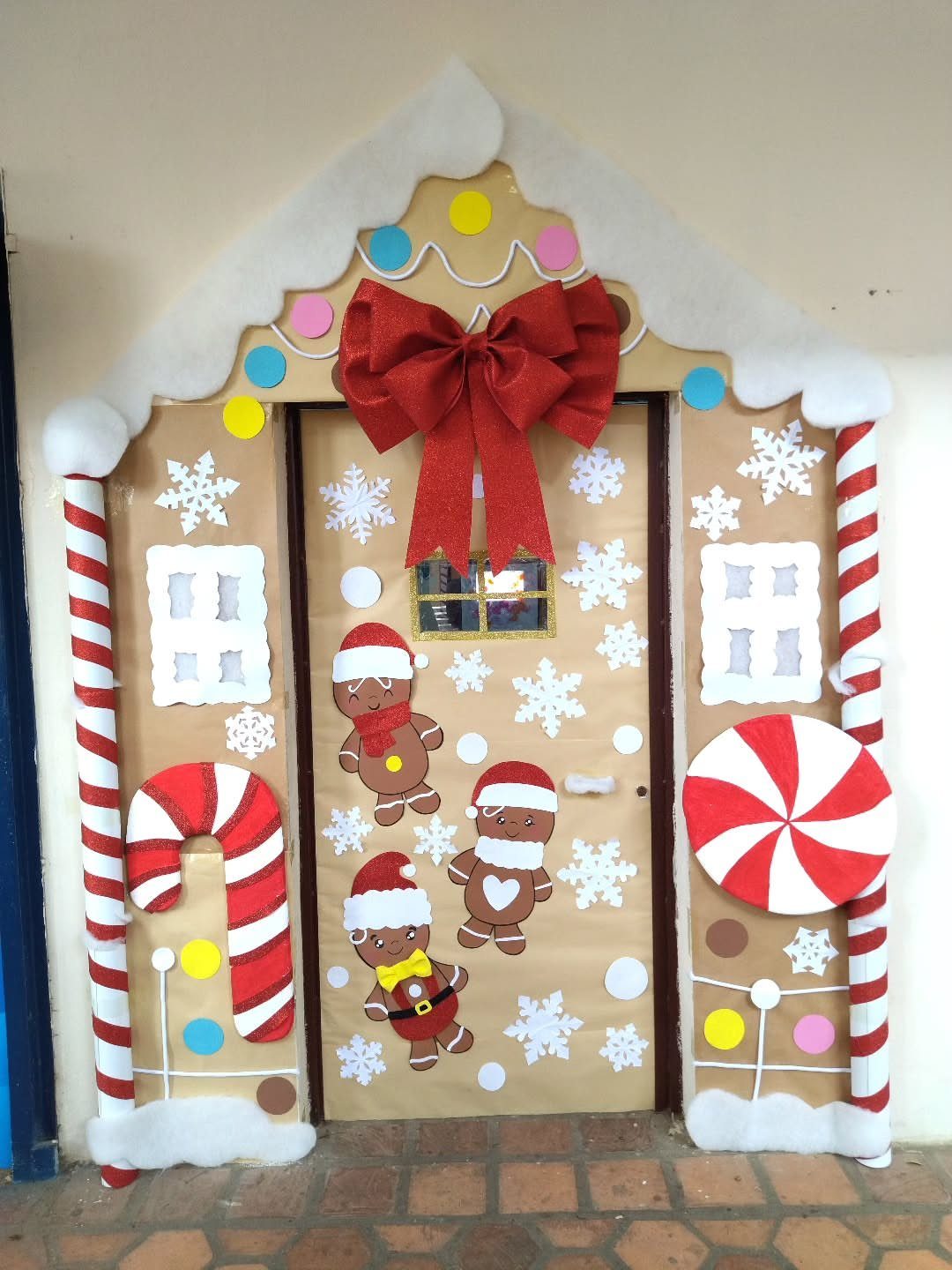 16 Christmas Decorations for Office Spaces That Shine 3 Door decorated as a gingerbread house with candy canes, snowflakes, and a red bow.