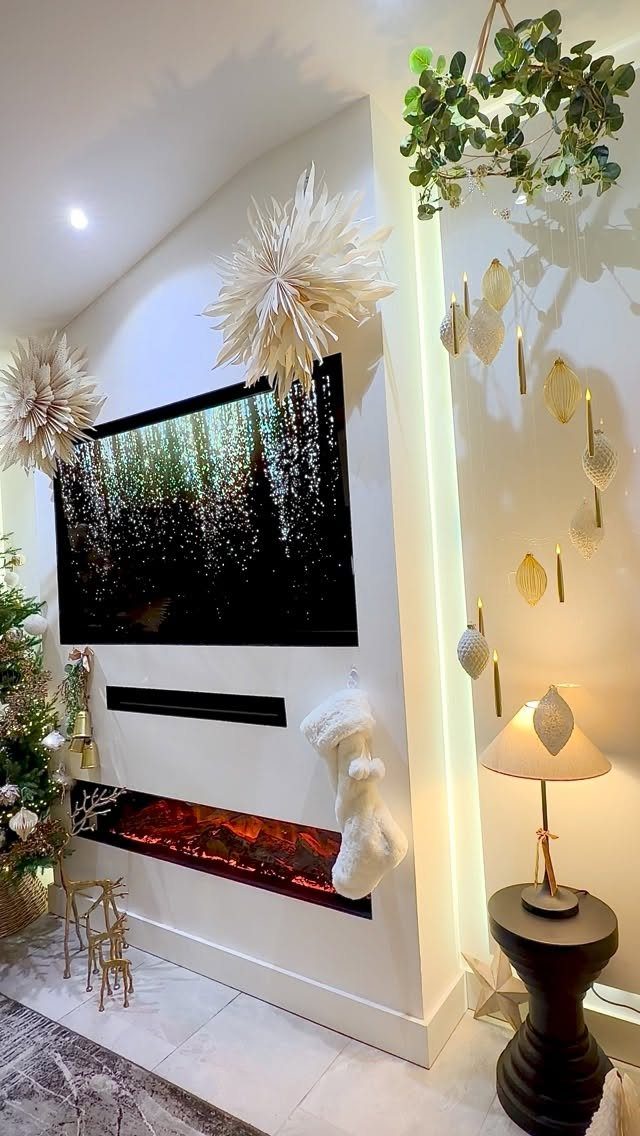Modern living room with electric fireplace, white stocking, and festive gold wall decorations.