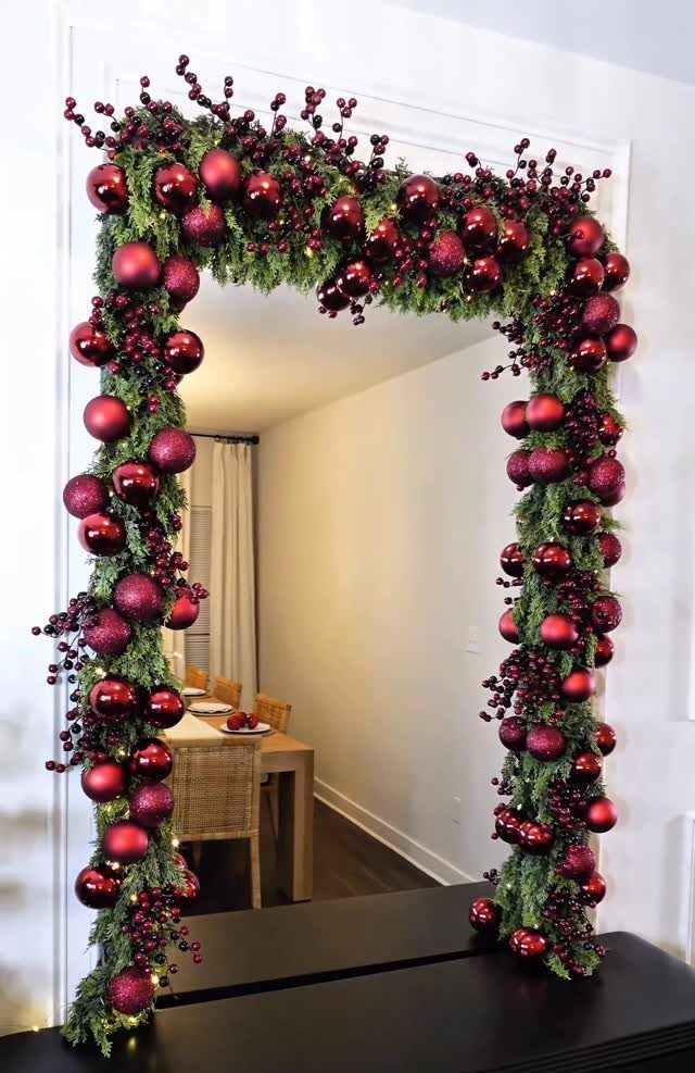 Mirror framed with a green evergreen garland and red Christmas ornaments in a room.