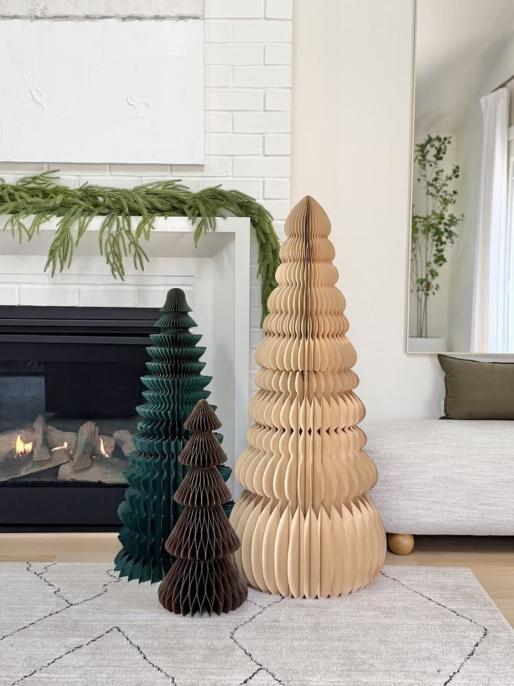 Three pleated cardboard Christmas trees standing on a light grey patterned area rug.