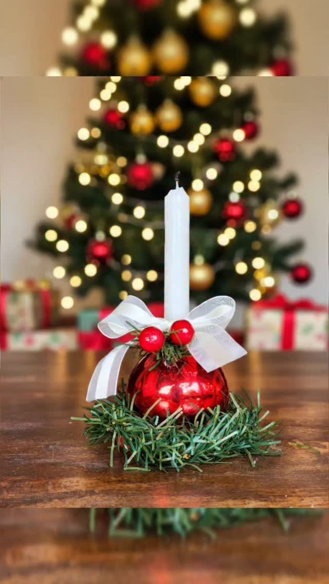 Red ornament candle holder with white bow on a wooden table near Christmas tree.