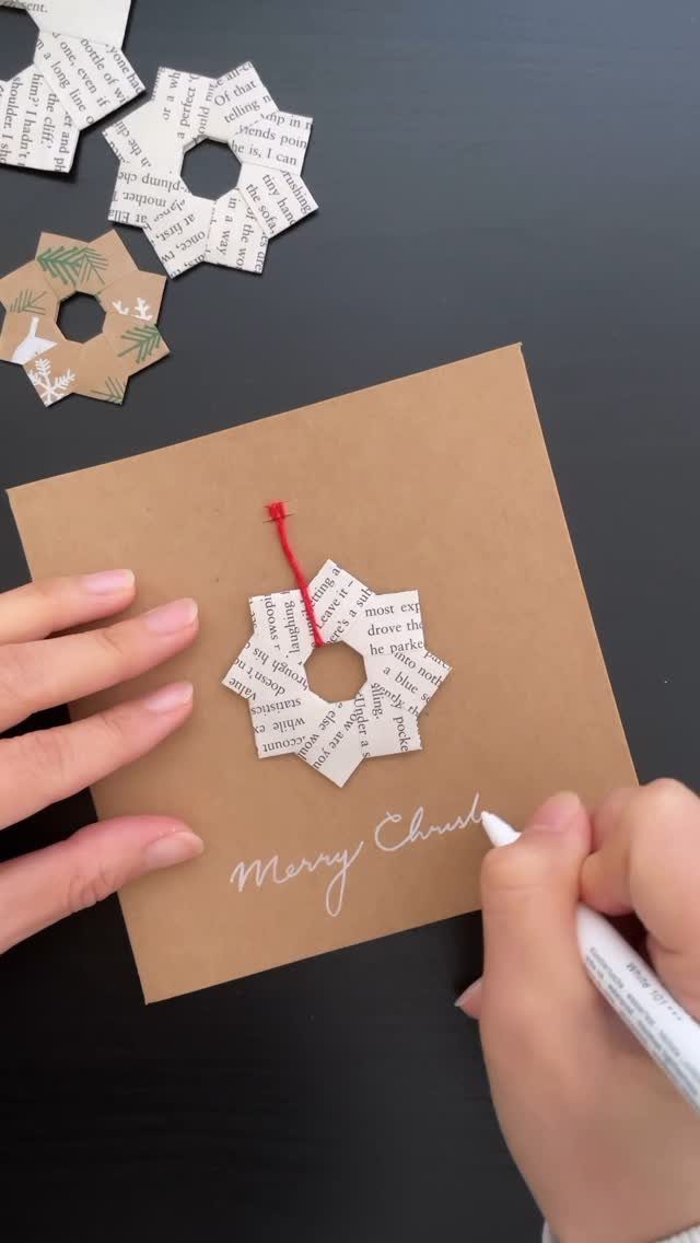 20 Christmas Decorations to Make at Home in 2026 5 Hands writing on a brown card decorated with a newsprint paper star ornament.