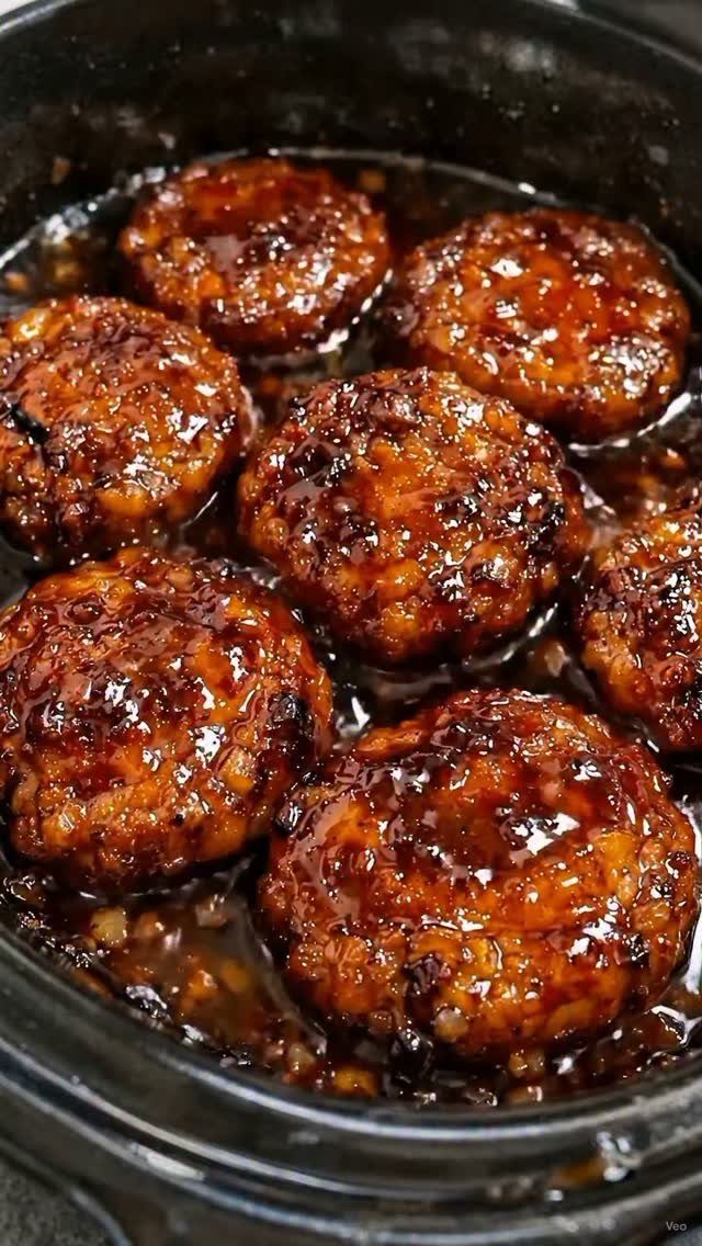15 Christmas Dinner Party Ideas for a Festive Celebration 12 Glazed meatballs simmering in a dark sauce inside a black slow cooker.