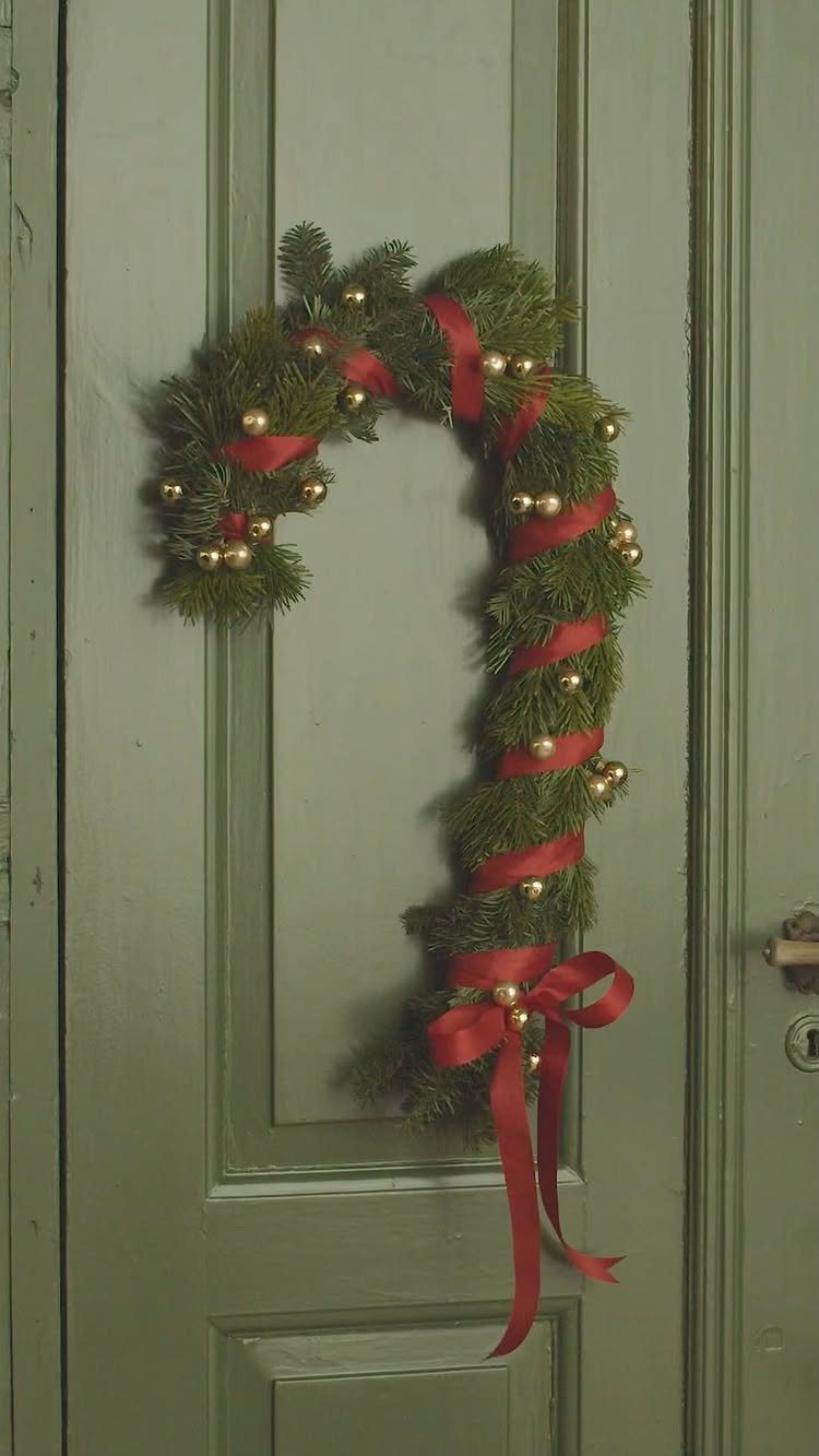 33 Christmas Party Decor Ideas to Bring the Holiday Magic 20 Candy cane shaped evergreen wreath with red ribbon and gold ornaments on a door