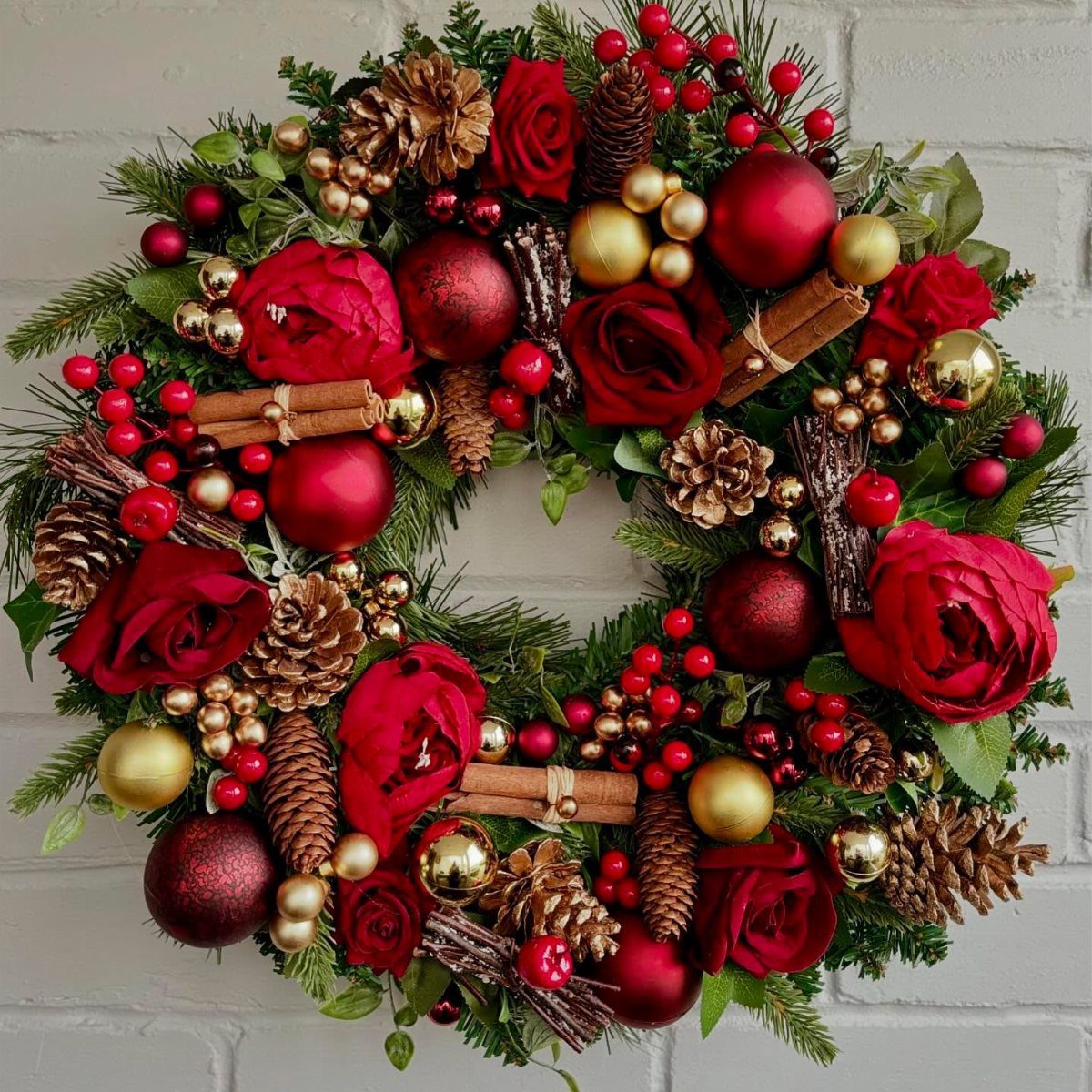 33 Christmas Party Decor Ideas to Bring the Holiday Magic 1 Christmas wreath with red roses, gold and red ornaments, and pinecones on white brick.