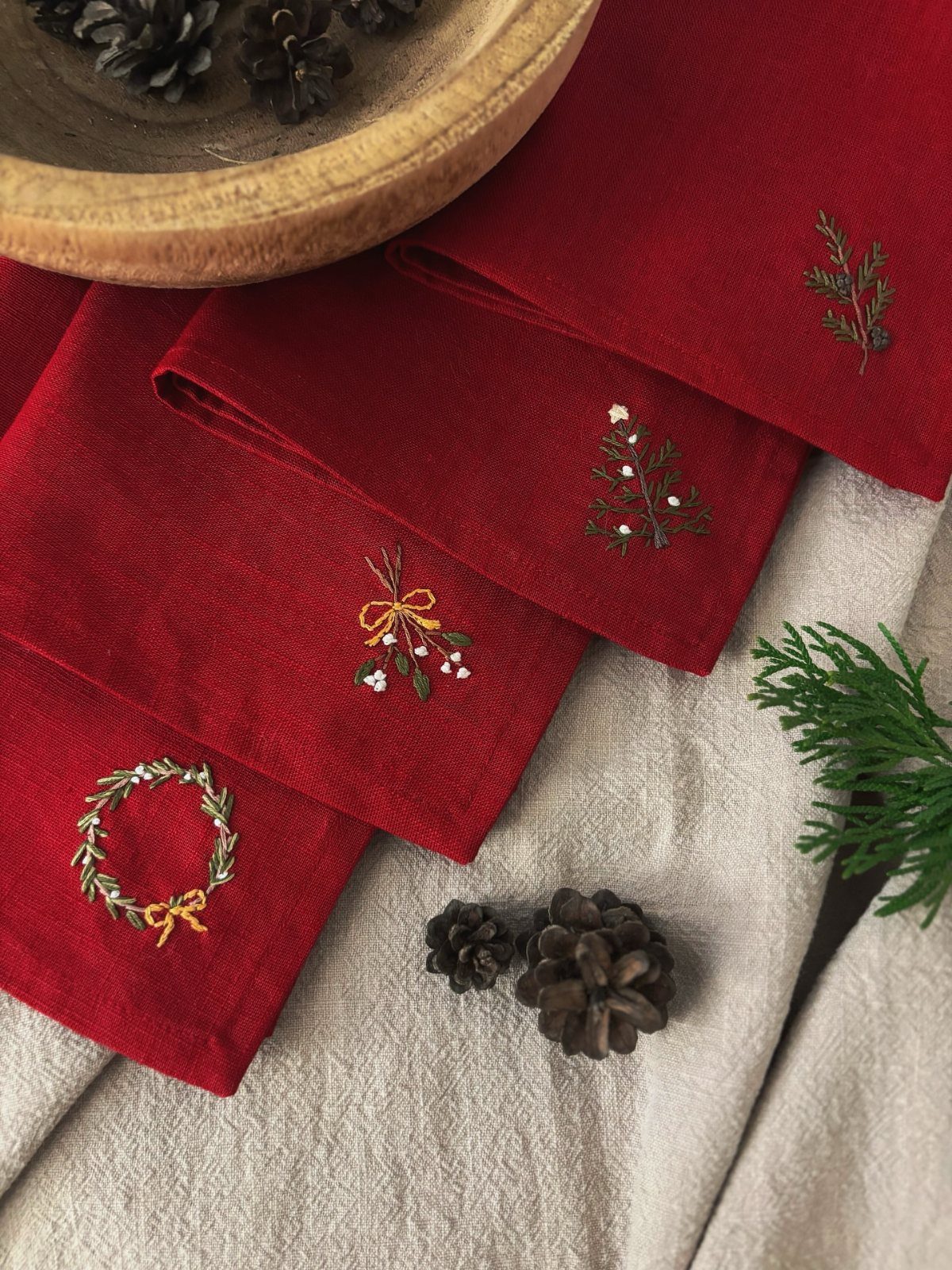 33 Christmas Party Decor Ideas to Bring the Holiday Magic 13 Red fabric napkins with embroidered Christmas wreaths and pine branches on a beige cloth.