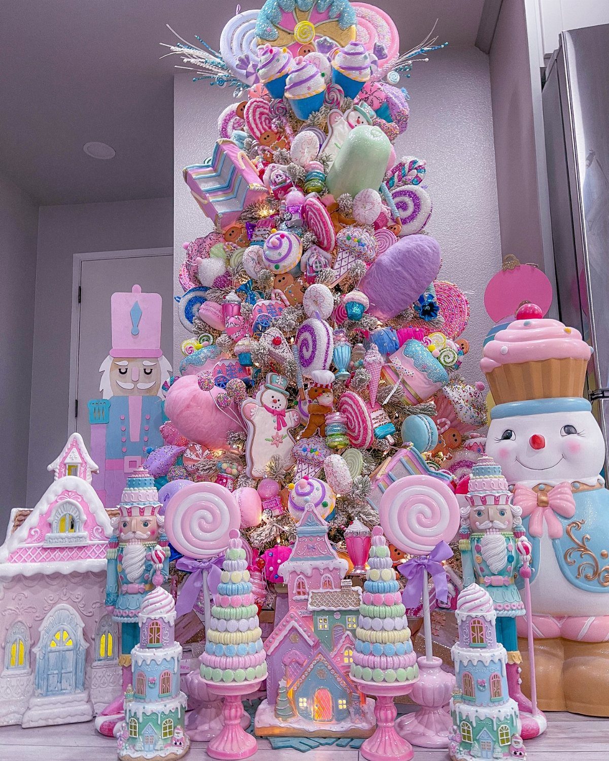 Pastel Christmas tree decorated with oversized candy and cupcakes surrounded by whimsical gingerbread houses.