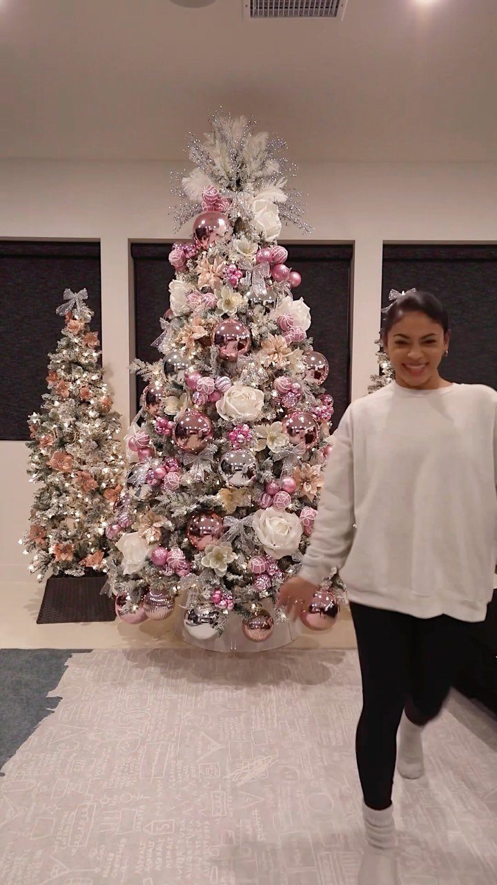 Woman standing beside a Christmas tree decorated with pink and silver ornaments and flowers.