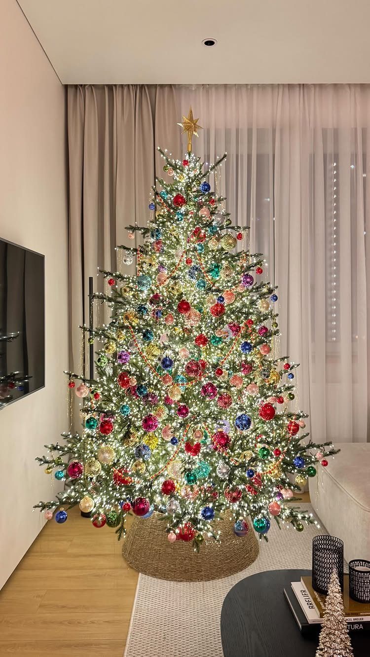 Multi-colored Christmas tree with rainbow ornaments and a gold star in a modern room.
