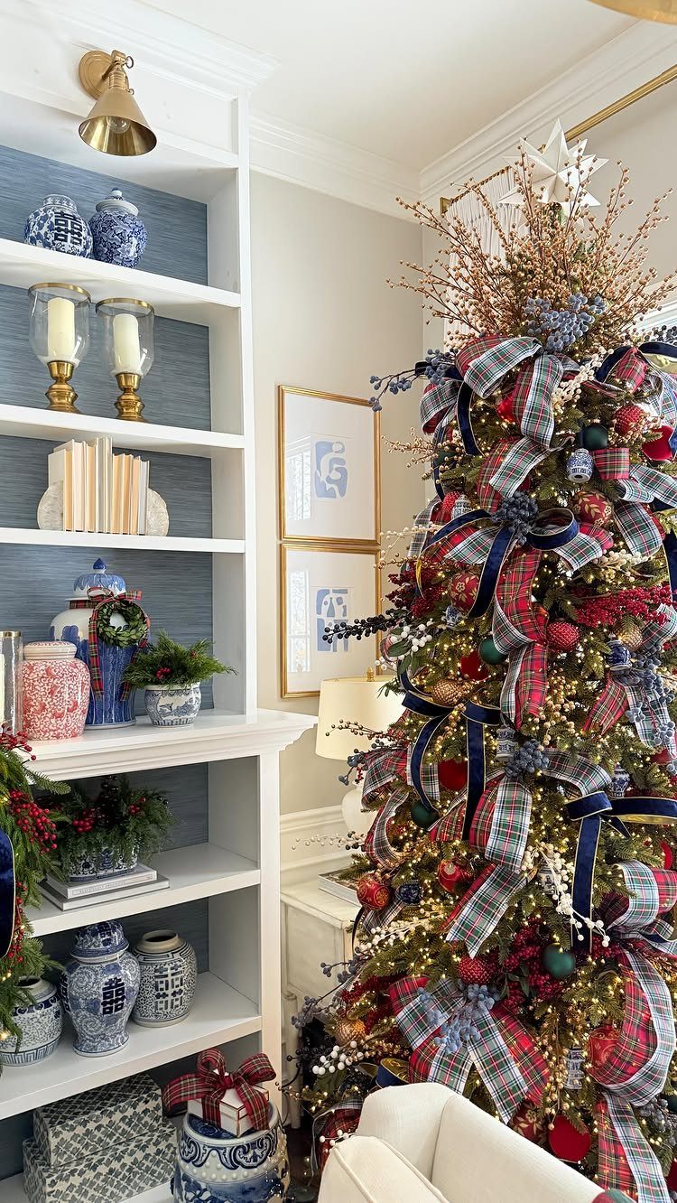 Christmas tree decorated with red and blue plaid ribbons next to white shelves.