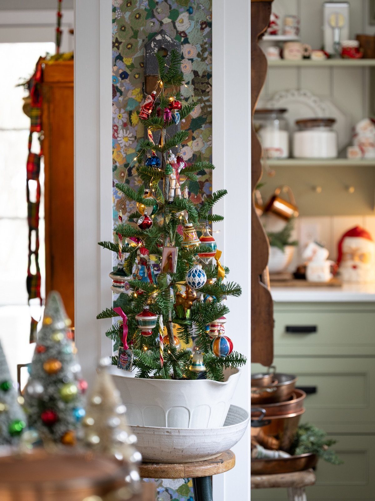 5 Christmas Tree in Kitchen Ideas with Photos 1 Small decorated Christmas tree in a white pot on a wooden kitchen stool.