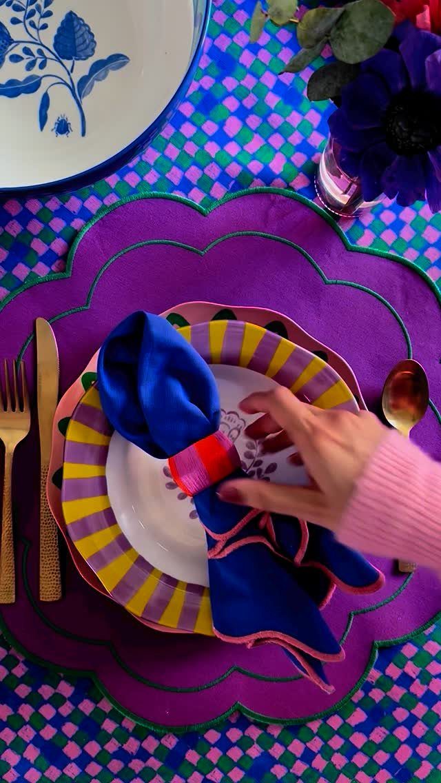 13 Contemporary Dining Room Decor Ideas for 2026 10 Colorful place setting with striped plates, blue napkin, and purple scalloped placemat.