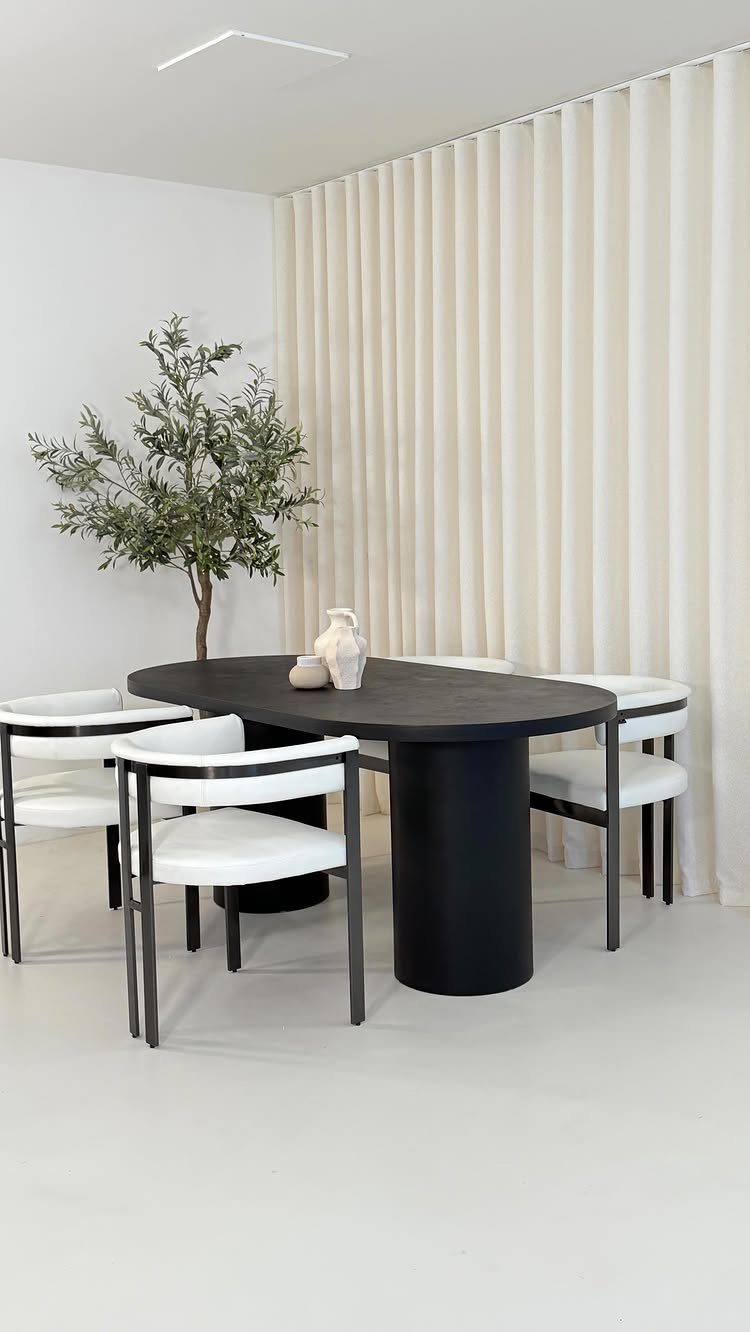 13 Contemporary Dining Room Decor Ideas for 2026 5 Black oval dining table with white chairs and a potted olive tree indoors.