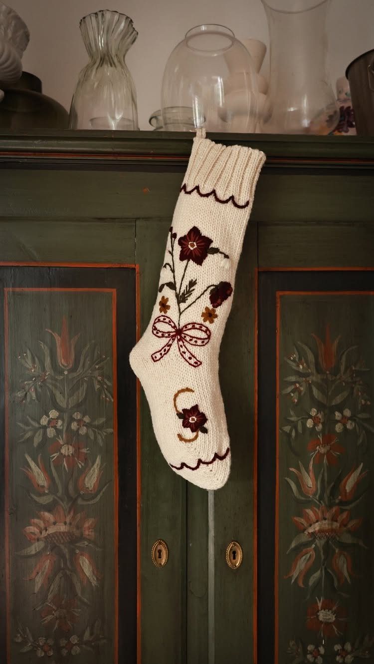 8 Cozy Christmas Bedroom Aesthetic Ideas to Try 3 Knitted cream Christmas stocking with red floral embroidery hanging on a green cabinet