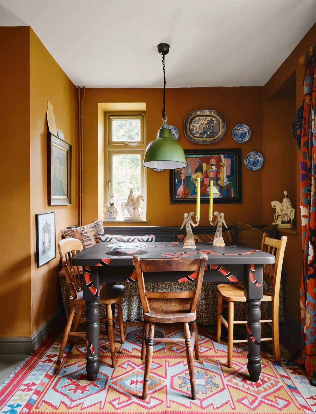 Eclectic dining room with ochre walls, patterned rug, and mismatched vintage wooden furniture.