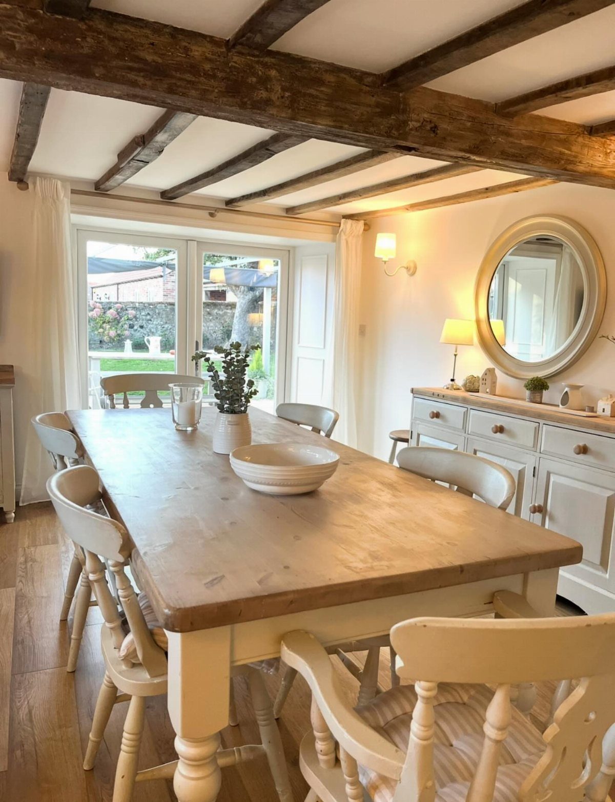 Rustic dining room with a wooden table, cream chairs, and exposed ceiling beams.
