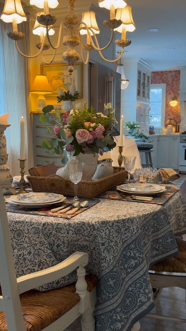 Dining table set with blue patterned cloth, brass candlesticks, and floral centerpiece.