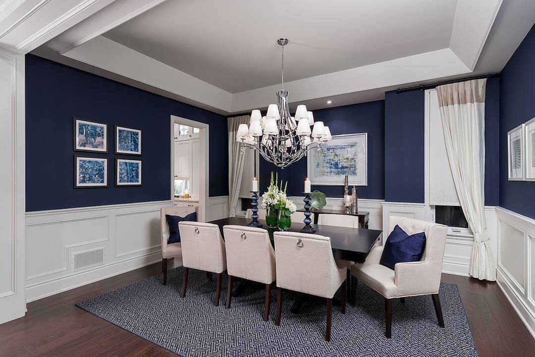 Cream upholstered dining chairs and dark wood table against dark blue walls.