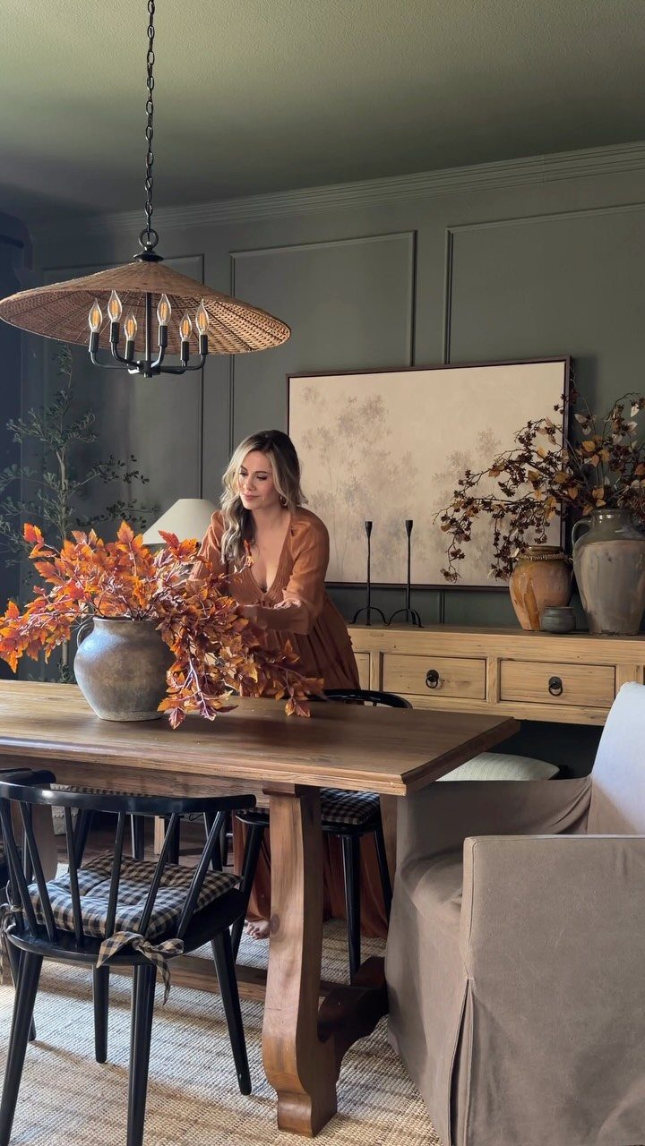 10 Ideas for Decorating a Dining Room Sideboard 3 Woman standing by a wooden sideboard decorated with vases and a painting.