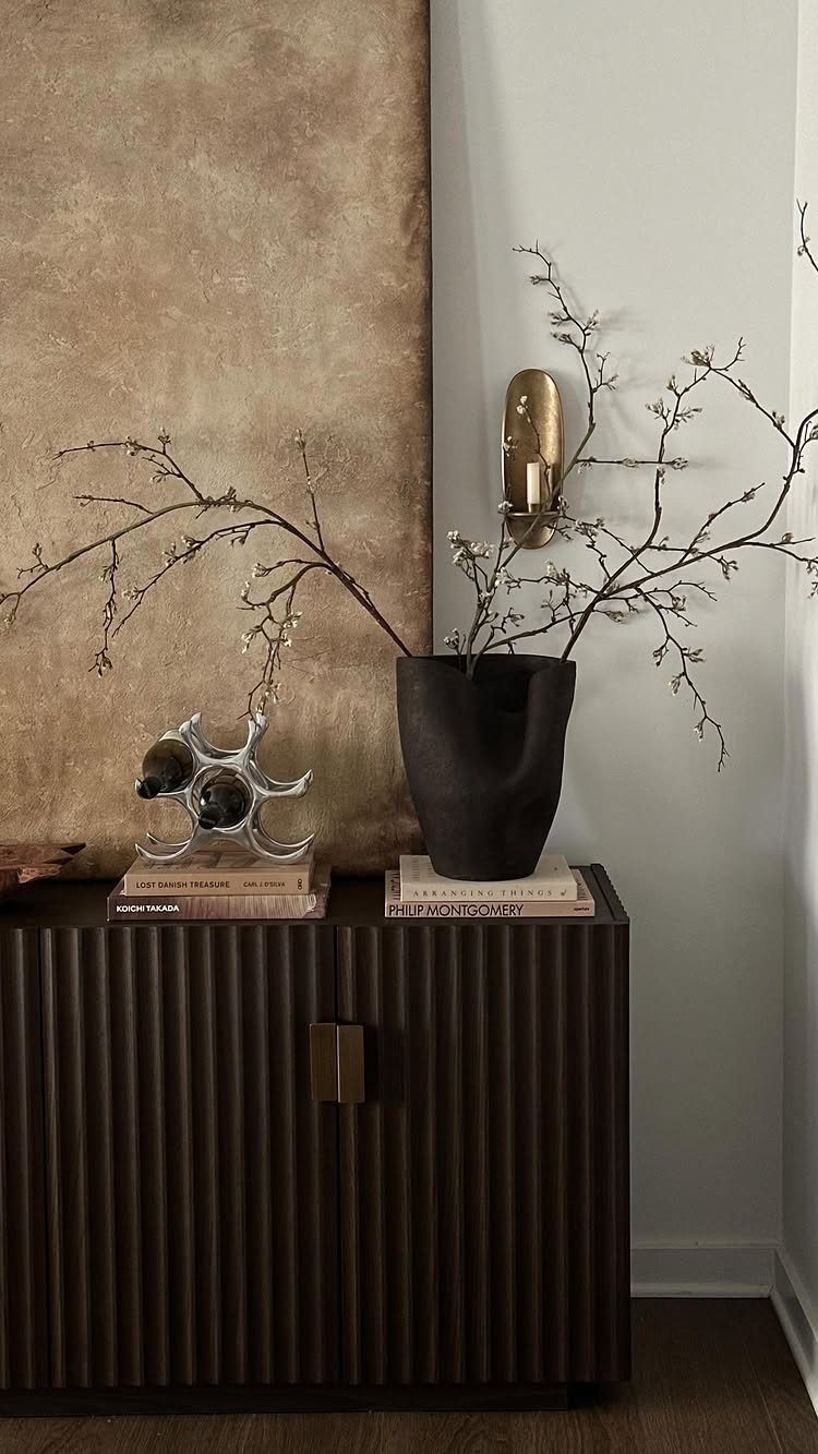 10 Ideas for Decorating a Dining Room Sideboard 7 Fluted dark wood sideboard decorated with a black vase, branches, and books.