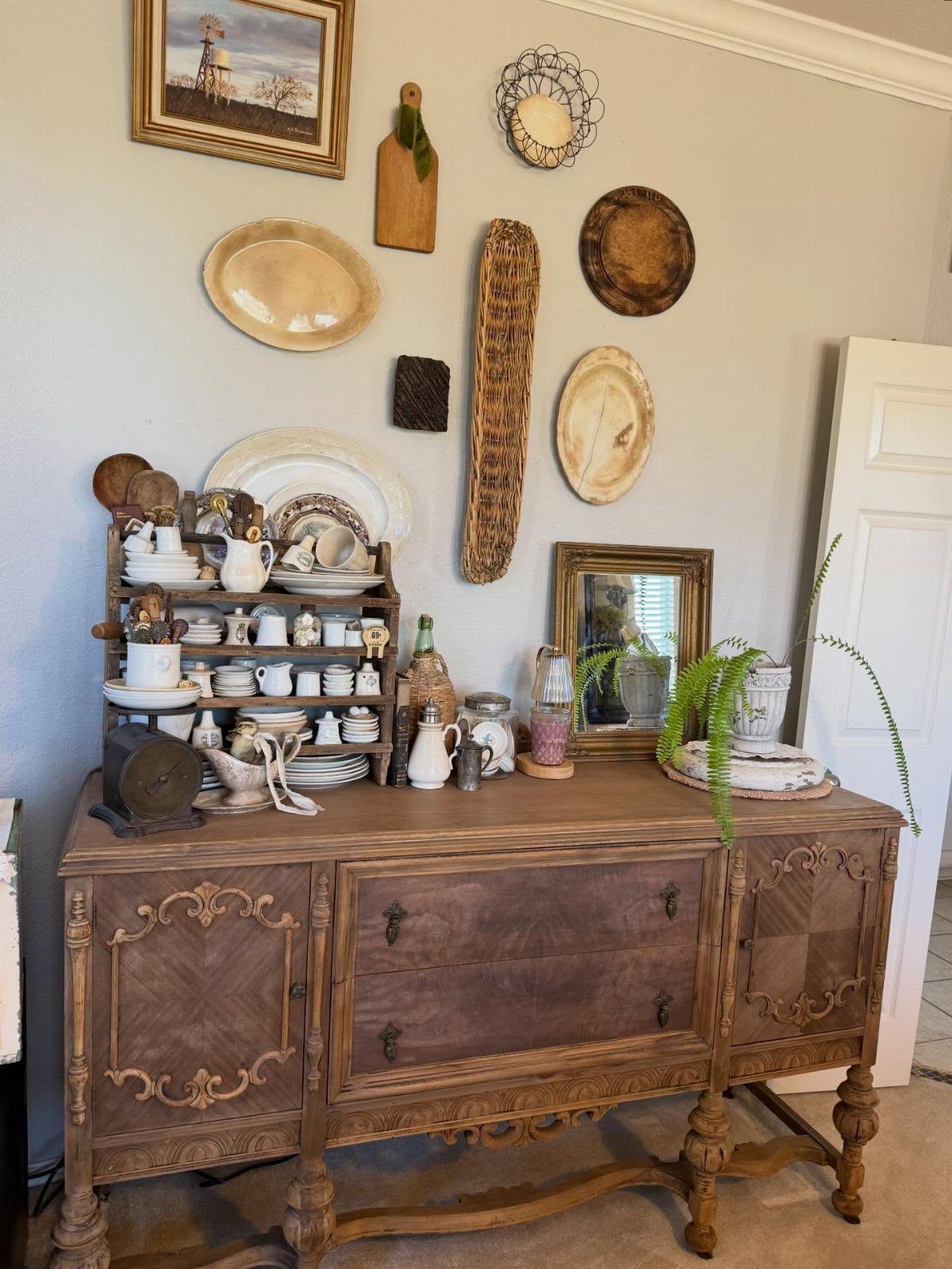Ornate wooden buffet with white ceramics and various wall art and platters above.