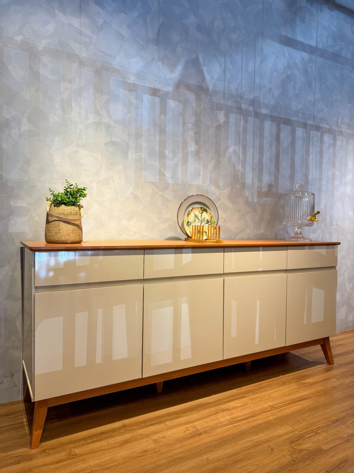 Modern beige buffet sideboard with a potted plant and decorative plate on top.