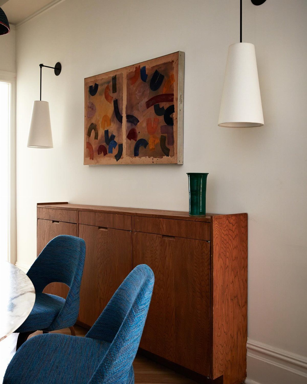 Wooden buffet with a green vase and abstract painting on a white wall.