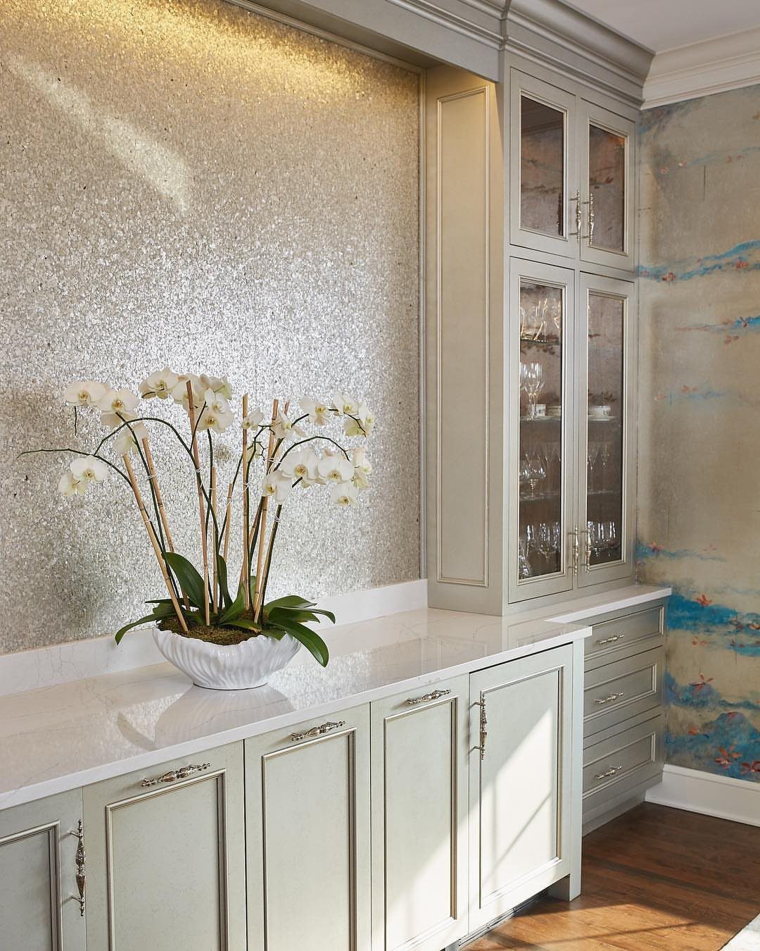 White dining room buffet with orchids against a shimmering gold textured wall.