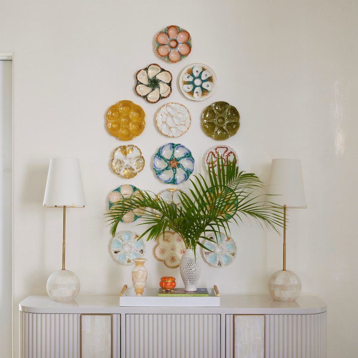 White textured vase with palm leaves on a white buffet table with lamps.
