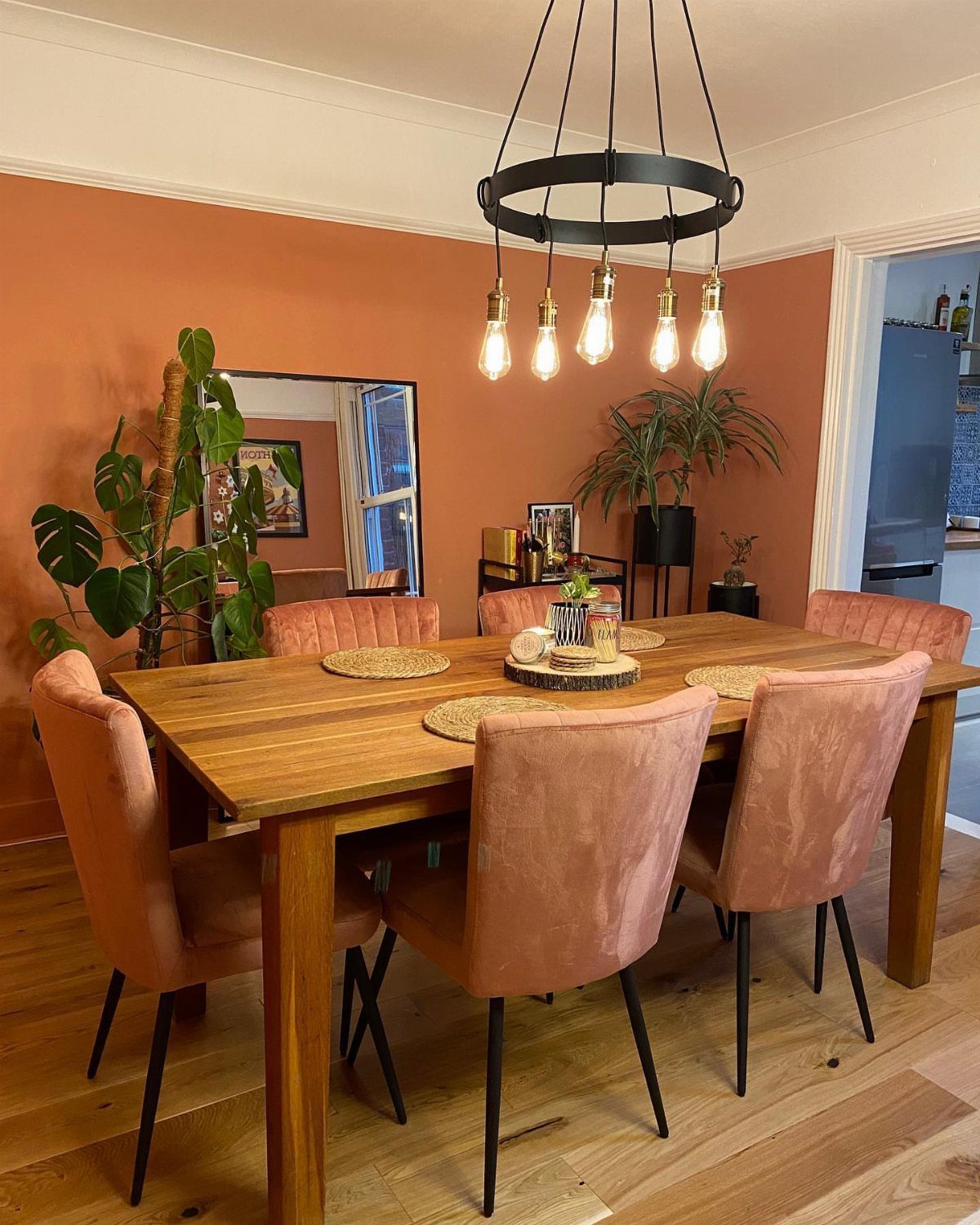10 Dining Room Colors for 2027 That Feel Fresh and Grounded 7 Dining room with terracotta orange walls, wooden table, and rose velvet chairs.
